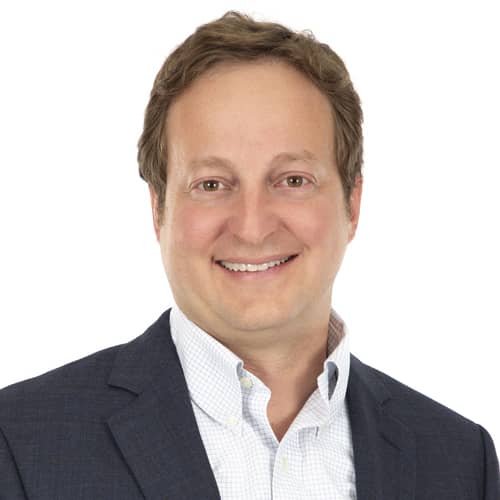 Person smiling in a suit and white shirt against a white background.